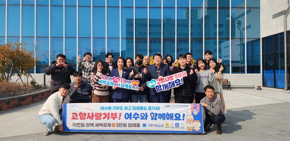 여수에서 고향사랑기부 캠페인에 참여한 사람들과 함께 기념사진을 찍고 있다. 배경에는 현대적인 건물이 보인다.