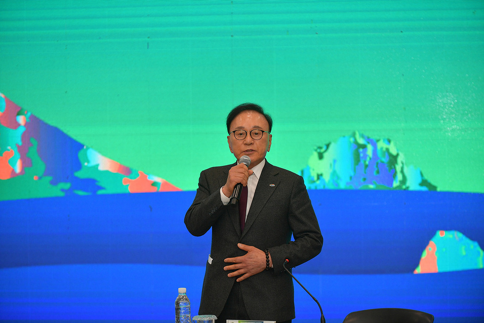 한 남성이 마이크를 들고 연설하고 있으며, 배경에는 추상적인 색상의 그래픽이 나타나 있다.