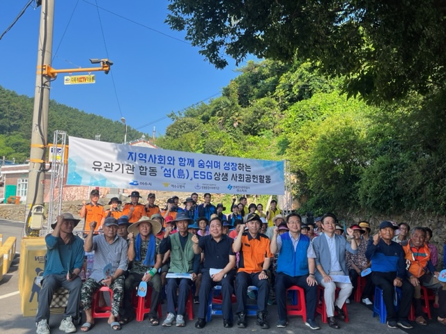 지역사회와 함께 숨쉬며 성장하는 유관기관 합동 '섬(島), ESG 상생 사회공헌활동 [여수시 /여수소방서 / 쌍봉종합사회복지관 /한국전기안전공사 여수지사] 현수막이 걸려 있고, 류갑선 복지교육국장과 주원영 여수소방서 예방안전과장, 김대연 한국전기안전공사 여수지사장, 김종진 쌍봉종합사회복지관장, 강성수 송도마을 이장, 마을주민 등 50여 명이 화이팅하는 포즈하고 있는 모습