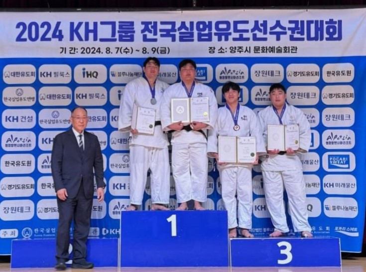 2024 KH그룹 전국실업유도선수권대회 기간 : 2024.8.7(수)~8.9(금) 장소 : 양주시 문화예술회관 대한유도회 | KH필룻그 | IHQ | 블루나눔재단 | 미래물산 | 동창동행시합리조트 | 장원테크 | 경기도유도회 | 한국유도원 | 한국실업류도연명 | 대한유도회 | KH필룩스 | 장원테크 | 경기도유도회 | KH건설 | 한국실업류도연맹 | 한유도회 | K | 장원테크 | 동창일반시합리조트 | KH | 연맹 | 대한 | 행정일반시화리조트 | 한국유도원 | 한국실업유 | 미래물산 | POCARI SWEAT | 경기도유도회 | 한국유 | KH | 나눔재단 | KH미래물산 | 장원테크 | 경기도 | 도원 | KH | Q | 블루나눔재단 |  주최: 한국실업협회| 주관 KH필룩스 사단법인블루나눔재단, 경기도유도회 포카리웨트 현수막이 걸려있고, 그 앞에 양복입은 한 남성과 1,3등이 유도복을 입은 4명의 선수가 상장을 들고 사진을 찍은 모습