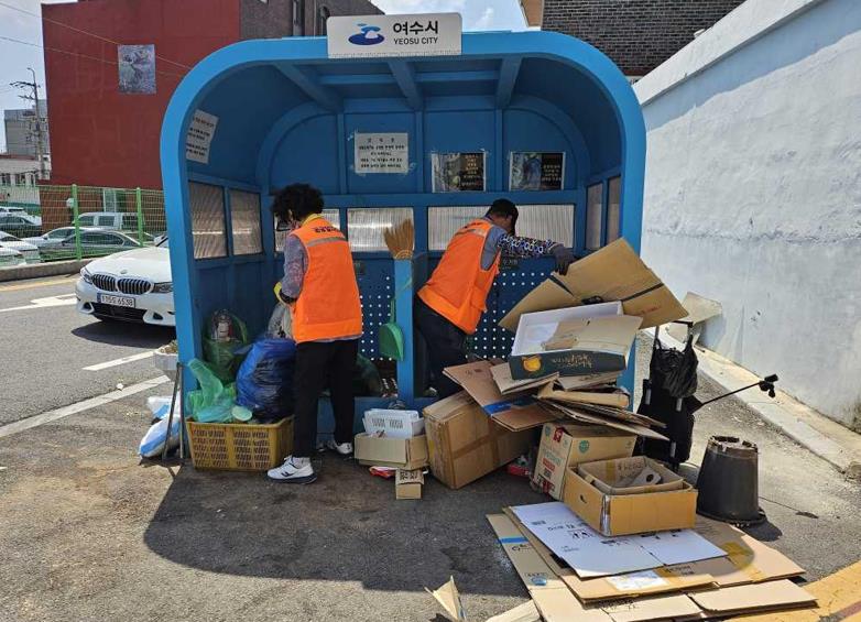 여수시의 한 쓰레기 수거 장소에서 두 명의 작업자가 쓰레기를 정리하고 있는 모습이다.