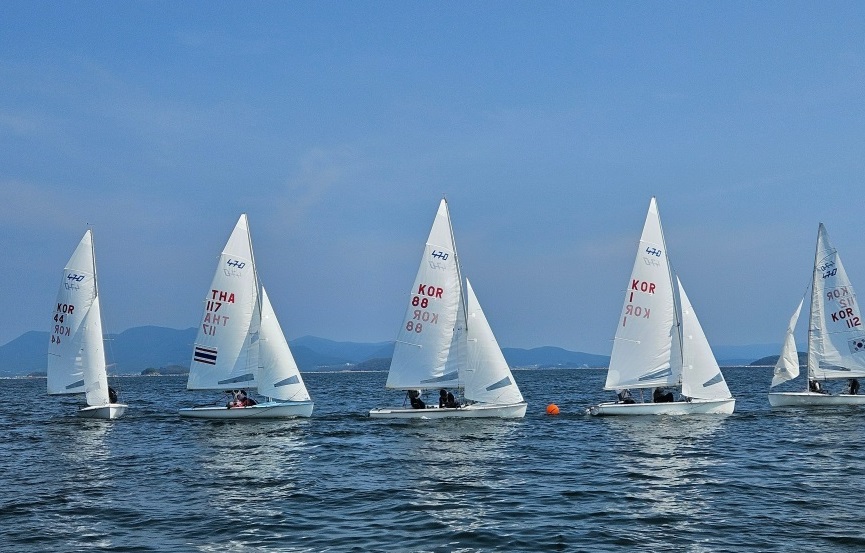 여수 앞바다에서 요트 선수들이 470급 요트를 타고 줄지어 항해하는 모습. 맑은 하늘 아래 여러 대의 요트가 바람을 받아 레이스를 펼치고 있다