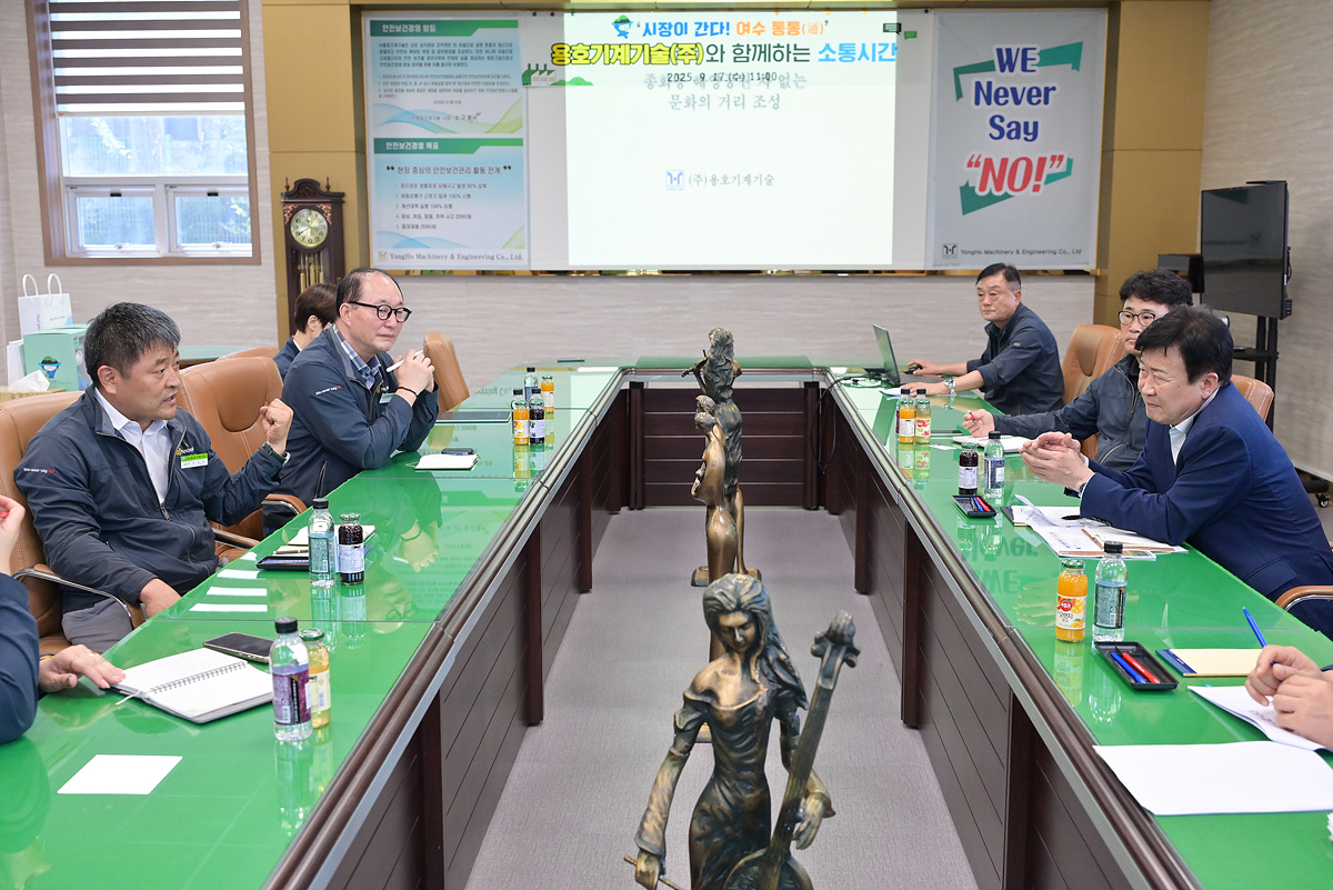 여수시장이 용호기계기술㈜ 회의실에서 기업 관계자들과 마주 앉아 소통 간담회를 진행하는 모습으로 테이블 중앙에는 조형물이 배치되어 있고 여러 음료가 놓여 있는 풍경.