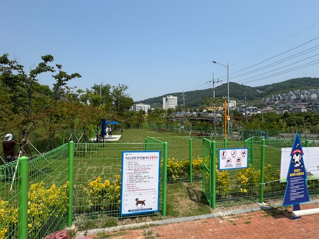 이순신공원 반려견놀이터 입구 전경으로, 초록색 철제 울타리 안에 잔디와 놀이 공간이 보이며 안내판과 이용수칙 표지판이 설치되어 있다.