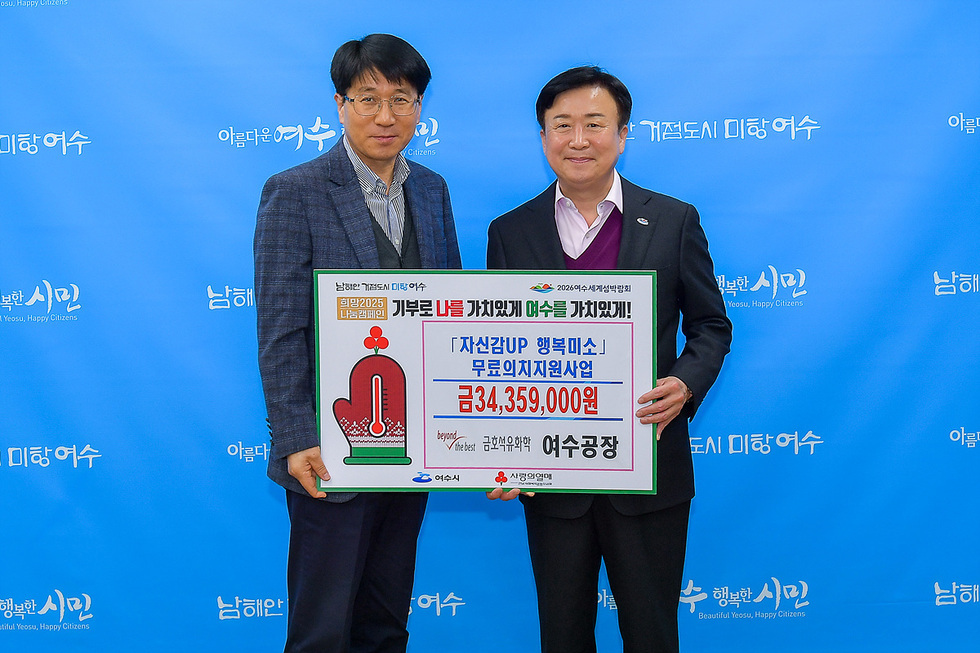 두 남성이 여수시청 배경 앞에서 자선사업에 대한 기부금 전달식을 진행하고 있다. 한 남성이 기부금 액수를 적은 현수막을 들고 있다.