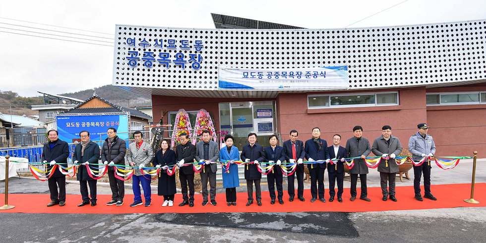 여수시 묘도동 공중목욕장 준공식에서 여러 인사들이 리본을 자르고 있다. 배경에는 새로 지어진 목욕장 건물이 보인다.
