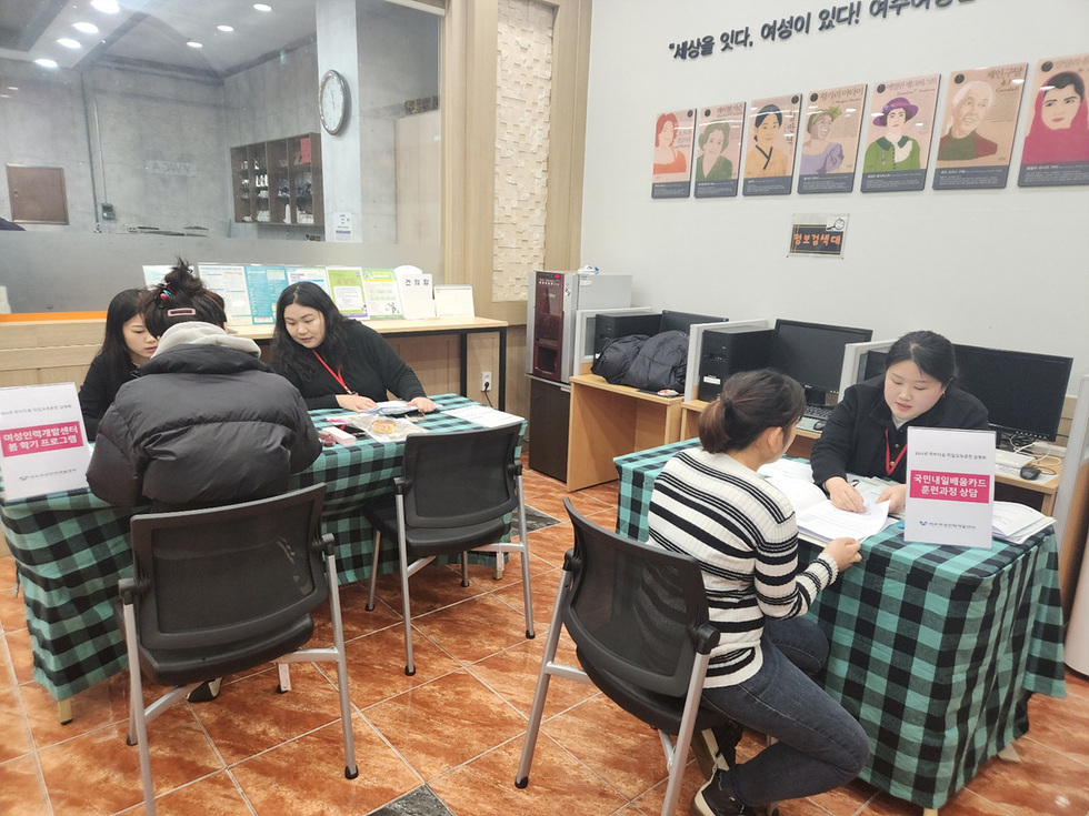 여성인력개발센터에서 두 명의 상담사가 한 여성과 상담을 진행하고 있으며, 테이블 위에는 출산하기 프로그램과 국민내일배움카드 신청 상담 안내가 있다.