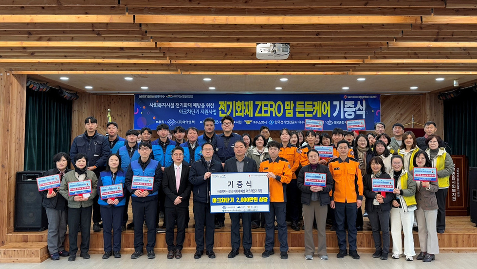 전기화재 예방을 위한 기증식에서 여러 사람들이 기념사진을 찍고 있으며, 배경에는 관련 현수막이 걸려 있다.