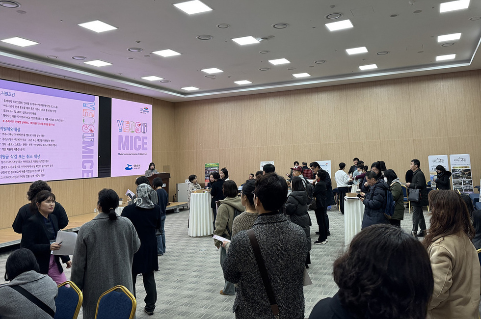 여수 MICE 행사에서 사람들이 발표를 듣고 있으며, 화면에는 여수 MICE 관련 정보가 표시되고 있다.