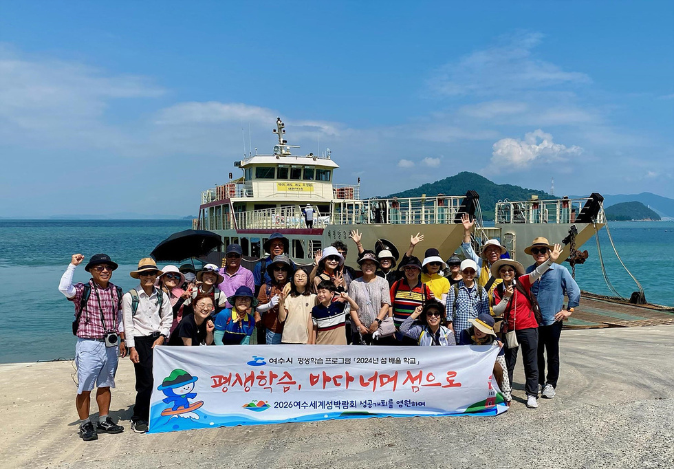 여수에서 평생학습 프로그램에 참여하는 사람들로 구성된 단체 사진으로, 배경에는 배와 바다가 보인다.