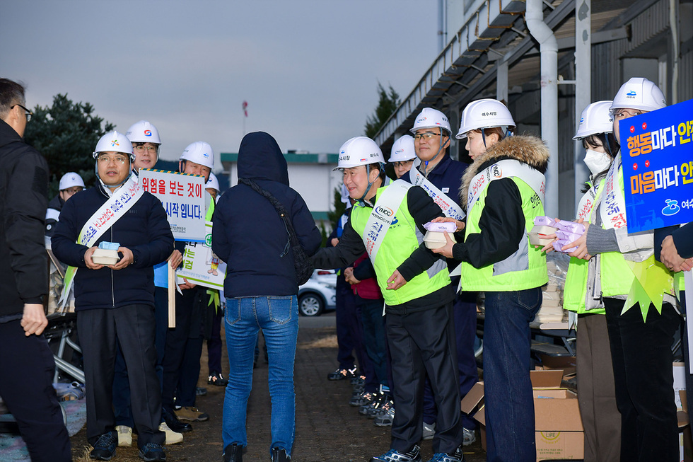안전모를 쓴 사람들이 위험 예방 캠페인에 참여하여 시민에게 안전 관련 정보를 전달하고 있다.