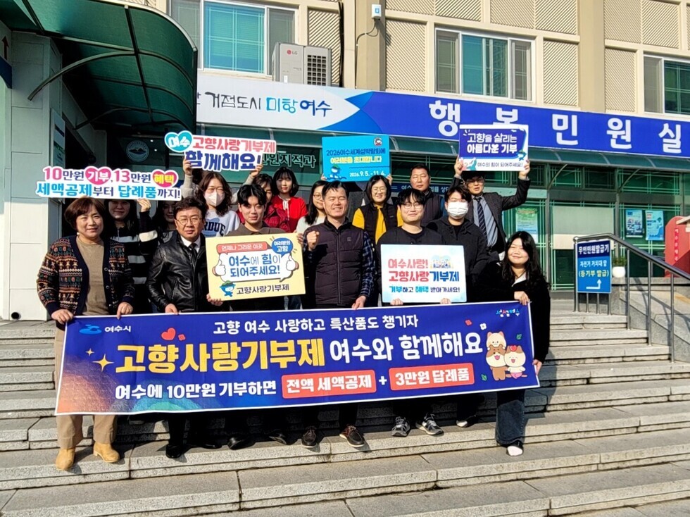 여수시청 앞에서 고향사랑기부제를 홍보하는 시민들이 모여있다. 그들은 기부를 독려하는 현수막과 팻말을 들고 있다.