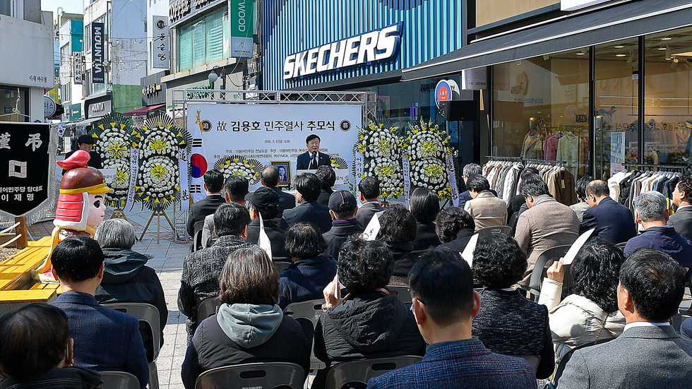 김용호 민주열사 추모식이 대전에서 열리고 있으며, 많은 사람들이 참석해 있다. 행사 중 한 연사가 발언하고 있고, 주변에는 조화가 놓여 있다.