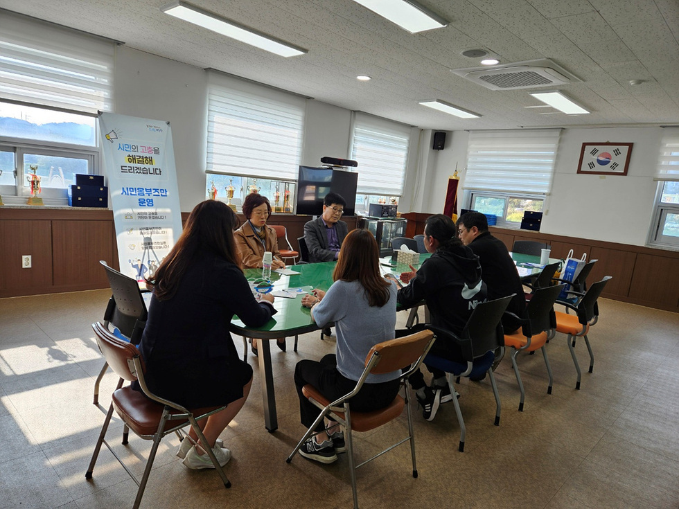 회의실에서 시민 복지 운영에 대한 논의가 진행되고 있는 장면으로, 테이블에 앉은 사람들이 대화하고 있다.