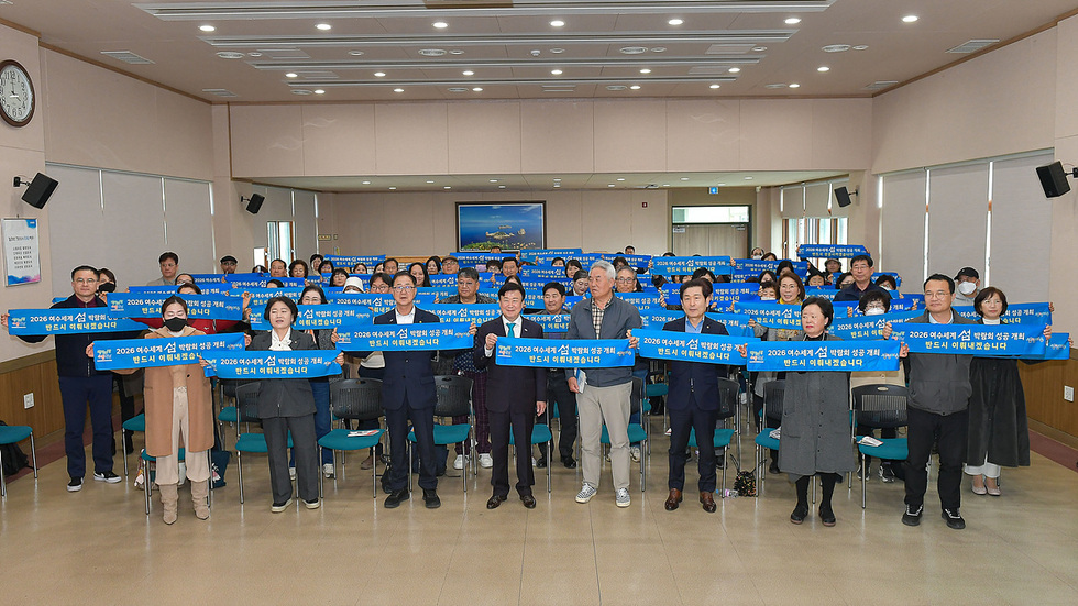 2026 아시안게임 유치 반대 캠페인에 참여한 사람들로 가득 찬 회의실에서 여러 명이 반대 현수막을 들고 있다.