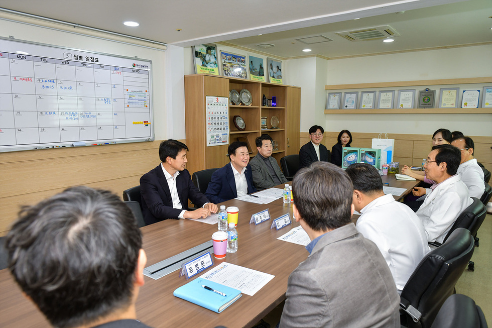 회의실에서 여러 명의 사람들이 모여 회의를 진행하고 있으며, 월별 일정표가 벽에 부착되어 있다.
