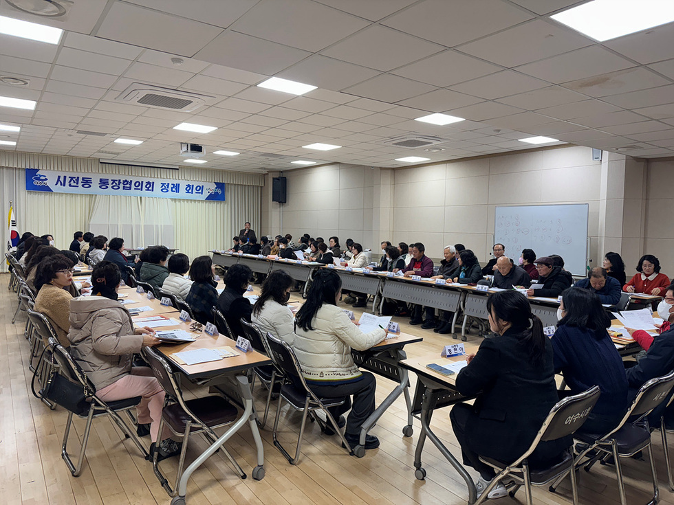 시전동 통장협의회 정례 회의가 진행되고 있는 모습으로, 많은 사람들이 테이블에 앉아 회의에 참석하고 있다.