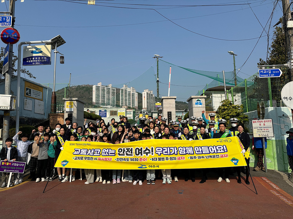 여수에서 학생들과 경찰이 함께 모여 교통안전 캠페인을 진행하는 모습으로, 큰 현수막이 교통사고 예방을 강조하고 있다.