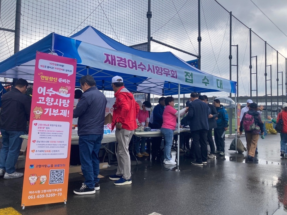 여수시 고향사랑 기부제를 홍보하는 부스에서 사람들이 접수하고 있는 장면이다. 부스에는 재경여수시향우회와 관련된 정보가 적힌 현수막이 걸려 있다.