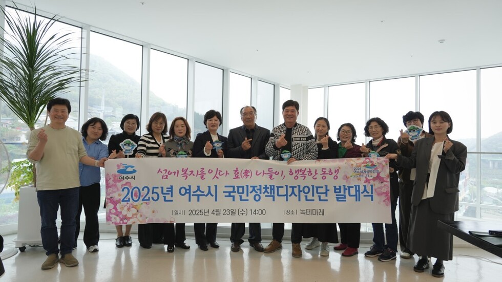 여수시 국민정책디자인단 발대식에서 단원들이 현수막을 들고 기념촬영하는 모습. 참석자들이 카메라를 향해 손가락 하트 포즈를 취하고 있다.