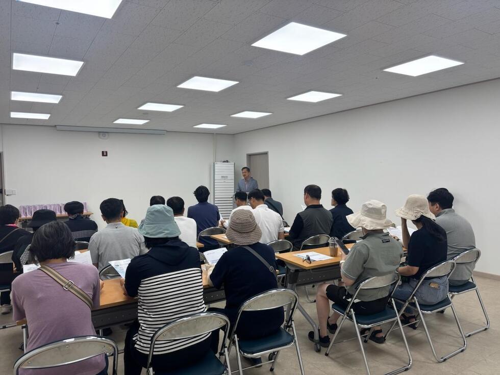 회의실에서 여러 사람이 앉아 강의를 듣고 있는 모습이다. 강사는 앞에서 발표를 하고 있으며, 참석자들은 노트와 자료를 참고하고 있다.