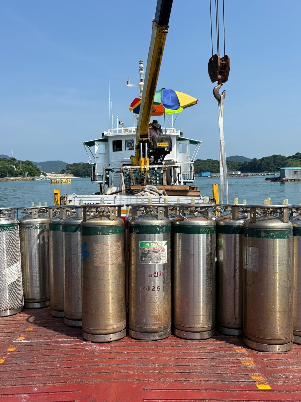 선박에서 크레인을 이용해 가스통을 옮기는 작업자가 보인다.
