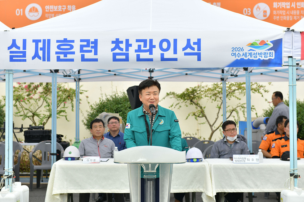 2026 여수세계섬박람회 관련 실제훈련에 참석한 관계자가 마이크를 들고 발언하고 있으며, 뒤에는 여러 관계자들이 앉아 있다.