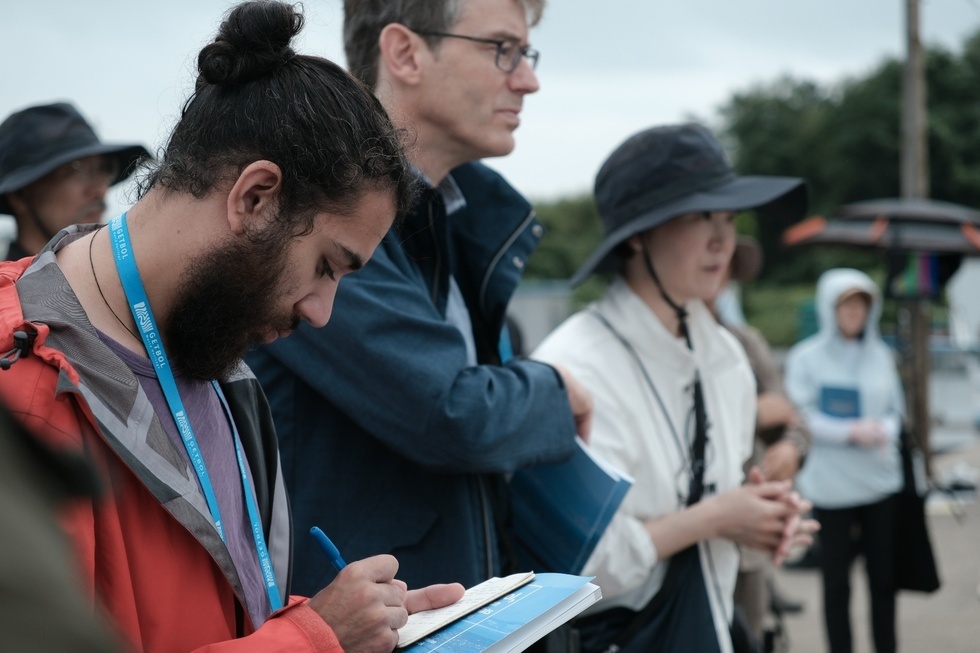 여수갯벌 현장실사에 참여한 전문가들이 조사 중인 모습으로, 한 남성이 메모를 하고 있으며 다른 참석자들이 뒤에 서 있다.