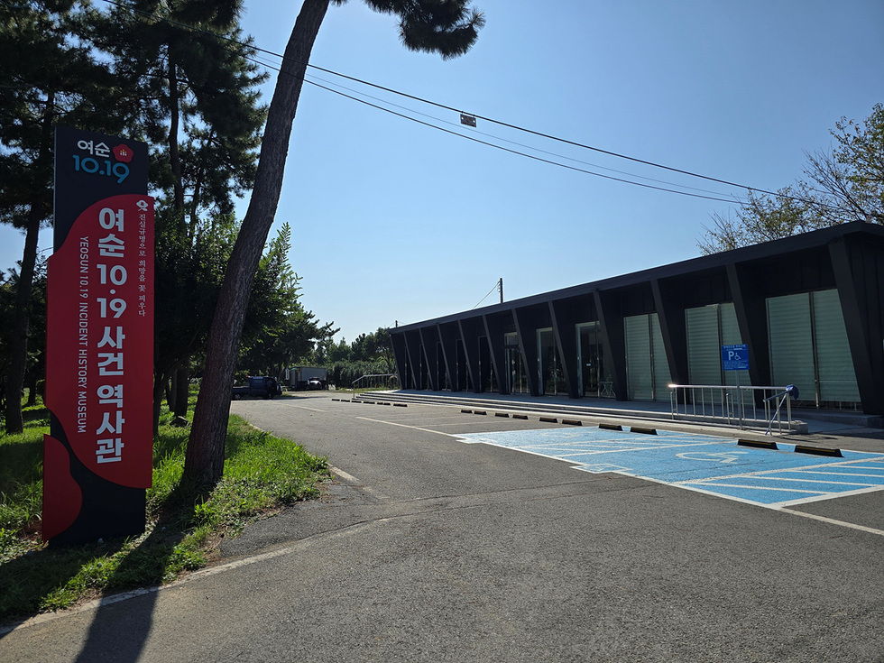 여순10.19사건 역사관의 외관이 보이는 장면으로, 건물 앞에 역사관을 알리는 큰 구조물이 설치되어 있다.
