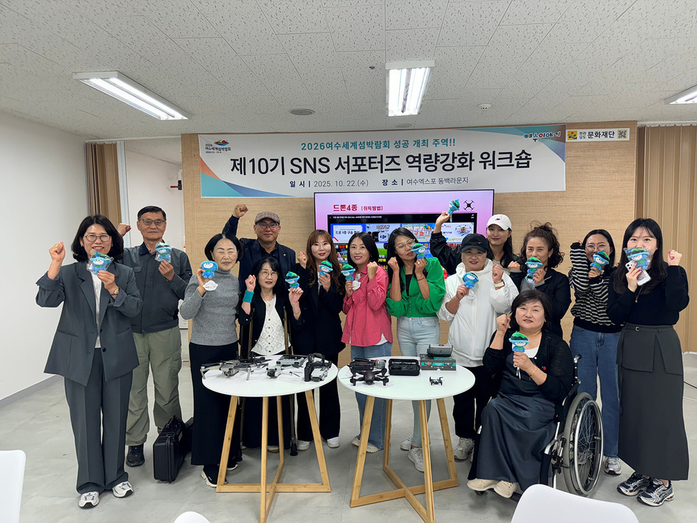 여수시 SNS 서포터즈가 드론 교육을 받으며 기념사진을 찍고 있는 모습으로, 워크숍에 참석한 참가자들이 드론과 기념품을 들고 있다.