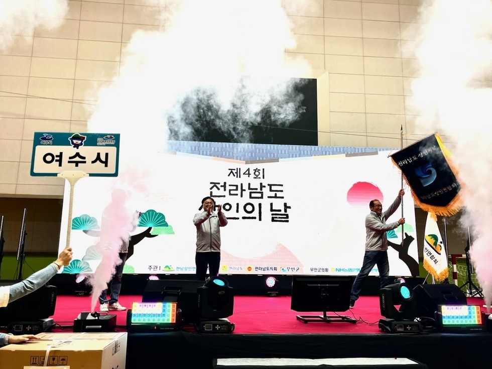 여수시에서 열린 제4회 전라남도 상인의 날 행사에서 한 사람이 마이크를 들고 연설를 하고 있으며, 다른 사람이 조직깃발을 흔들고 있다.