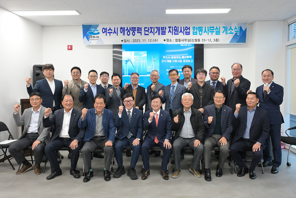 ‘여수시 해상풍력 단지개발 지원사업 합동사무실 개소식 일시: 2025년 11월 12일 (수) / 장소:합동사무실(신월동 33-12,3층)’이라고 적힌 현수막 앞에서 정기명 여수시장과 관계자들이 단체로 서서 주먹을 들어 올리며 기념촬영하는 모습.