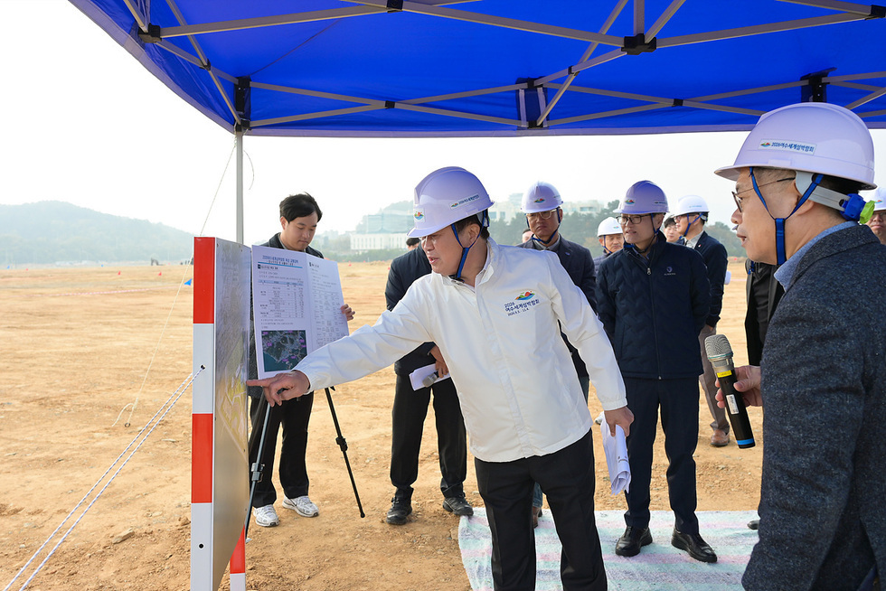 정기명 여수시장이 돌산 진모지구 2026여수세계섬박람회 주행사장 공사 현장을 찾아 관계자들과 현황판을 보며 조성 상황을 점검하는 모습. 모두 안전모를 착용한 채 기반시설 구축 현황을 브리핑하는 장면.