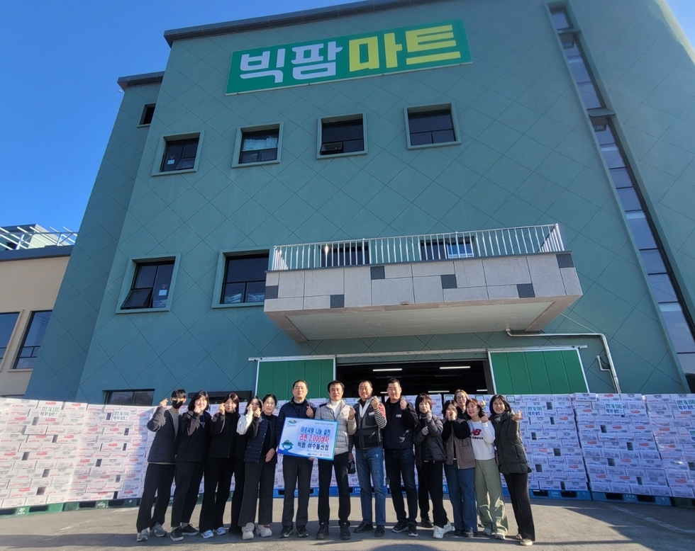 빅팜마트 건물 앞에서 관계자들이 기부 행사를 기념하며 함께 서서 사진을 찍고 있다. 중앙에는 라면 후원 안내문이 적힌 보드를 들고 있으며 주변에는 기부 물품 상자가 다수 쌓여 있다.