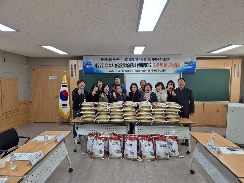 여수시농업인학습단체 한마음대회 기증용 쌀 나눔 행사장에서 관계자들이 쌀 포대가 쌓인 테이블 앞에서 단체 기념촬영을 하고 있는 모습