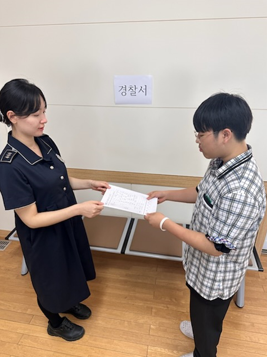 한 여성이 경찰서에서 남성에게 서류를 전달하고 있는 장면이다.