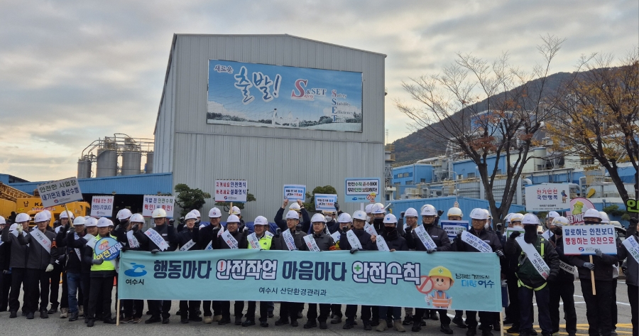 여수시 산업환경관리과” 문구가 적힌 현수막을 들고 산업단지 정문 앞에 모인 다수의 사람들이 안전캠페인에 참여해 서 있는 모습. 현수막에는 “행동마다 안전작업 마음마다 안전수칙”이라는 문구가 표시돼 있다.