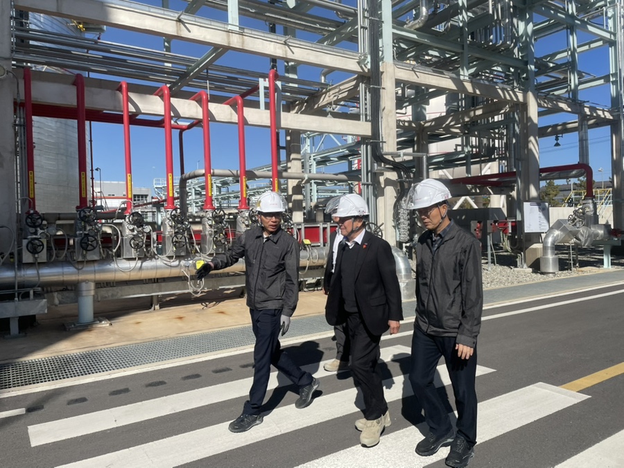 산업 현장에서 안전모와 작업복을 착용한 관계자들이 공장 배관시설을 배경으로 현장을 점검하며 이동하는 모습.