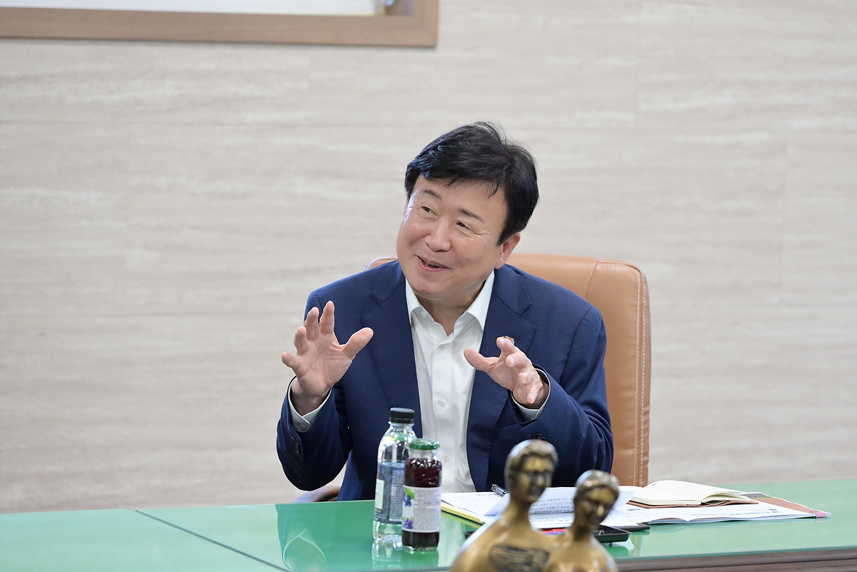 정기명 여수시장이 집무실에서 미소를 지으며 손짓을 하며 설명하는 모습으로 테이블 위에는 음료와 자료가 놓여 있는 상황