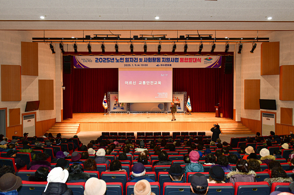 여수문화홀에서 2025년 노인 일자리 및 사회활동 지원사업 통합발대식이 열리고 있으며, 강연자가 어르신들을 대상으로 교통안전교육을 진행하고 있다.