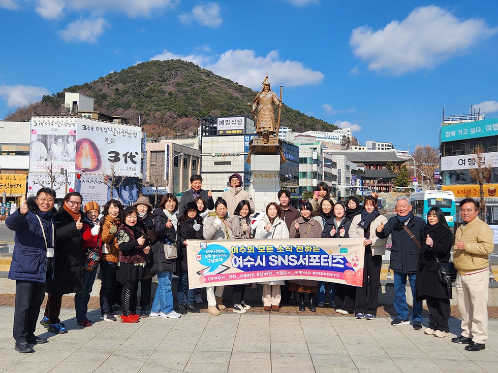 여수의 한 동상 앞에서 여수 SNS 서포터즈가 모여 기념사진을 찍고 있다. 참가자들은 손가락으로 엄지척을 하며 즐거운 분위기를 연출하고 있다.