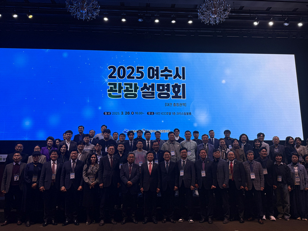 2025 여수시 관광 설명회를 위해 참석한 여러 사람들이 무대 앞에서 단체 사진을 찍고 있다. 배경에는 행사 정보가 적힌 대형 스크린이 있다.