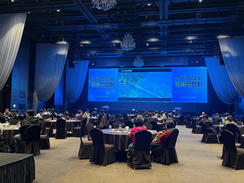2025 여수시 관광 설명회가 진행되고 있는 행사장 모습으로, 참석자들이 테이블에 앉아 발표를 듣고 있다.