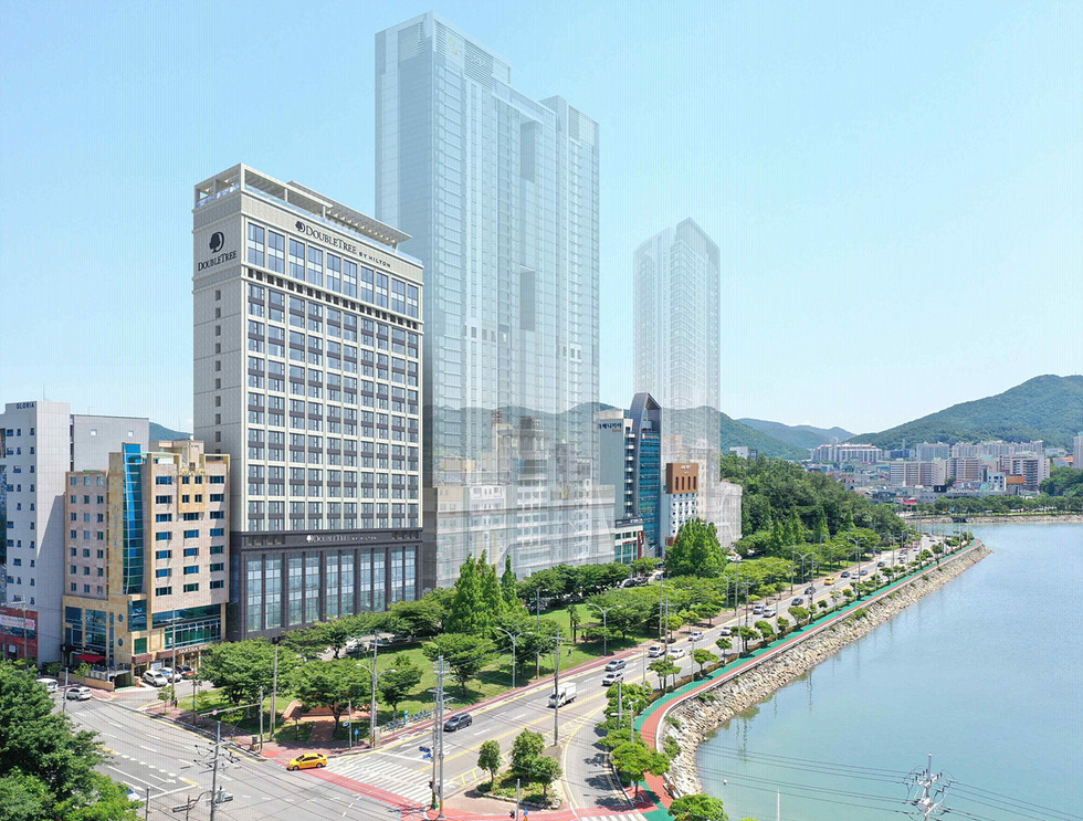 부산의 해안가에 위치한 더블트리 바이 힐튼 호텔과 주변 건물들이 보이는 풍경이다.