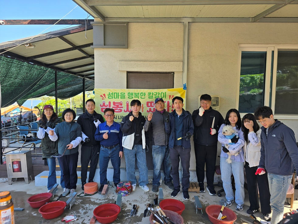 여러 사람이 섬마을에서 칼갈이 활동을 하며 기념사진을 찍고 있다. 배경에는 행사 관련 현수막이 걸려 있다.
