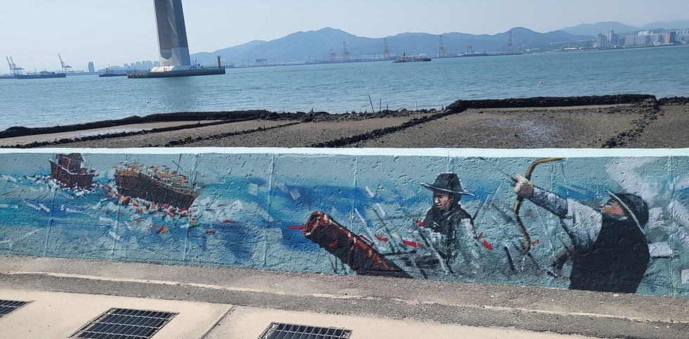 바다를 배경으로 한 벽화가 그려진 장면으로, 두 명의 인물이 어선과 함께 작업하는 모습이 담겨 있다.