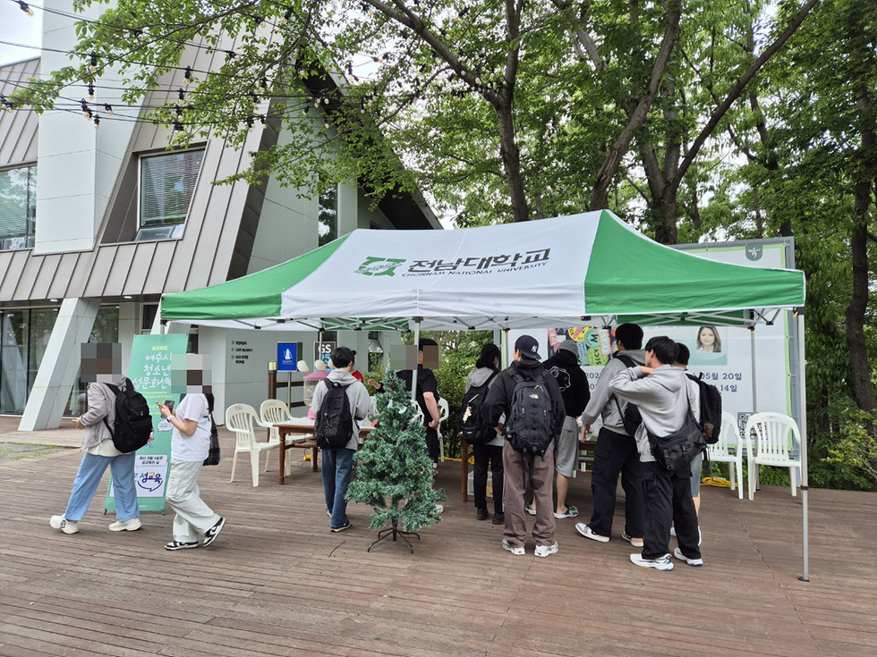 전남대학교의 텐트 아래에서 학생들이 모여 있는 모습으로, 텐트에는 전남대학교 로고가 보인다.