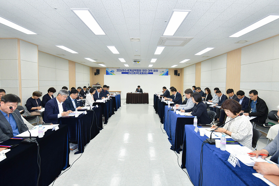 2026년 세계 설계 발전 회의에 참석한 여러 사람들로 구성된 회의 장면이다. 중앙에 있는 진행자가 회의를 이끌고 있으며, 참석자들은 메모를 하거나 자료를 보고 있다.