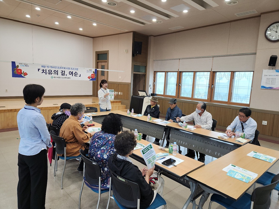 여성들이 모여 치유 프로그램에 참여하고 있는 모습으로, 한 강사가 자료를 들고 설명하고 있다.