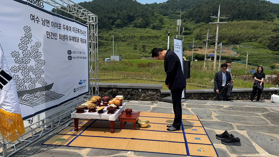 여수 남면에서 민간인 희생자 유해발굴 거행식이 진행되고 있으며, 한 남성이 제단 앞에서 고개를 숙이고 있다. 제단에는 과일과 전통 음식이 놓여 있다.